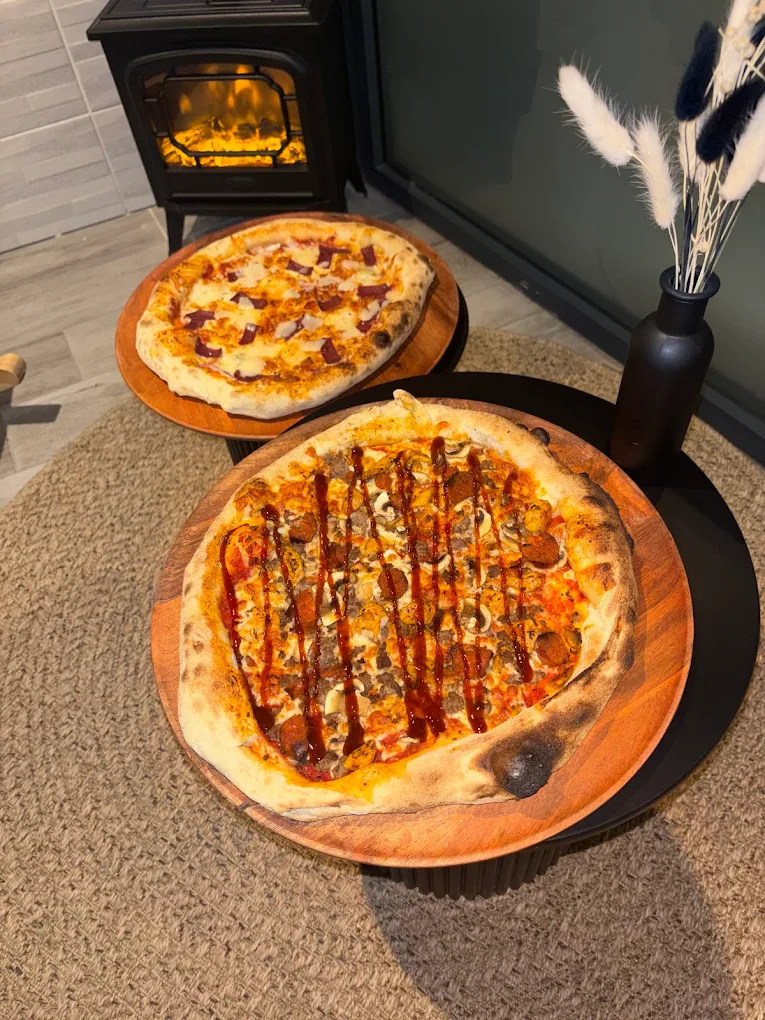 Deux pizzas sur planches en bois devant le poêle allumé, dont une nappée de filets de sauce barbecue